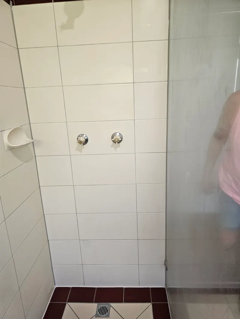 Tiled shower corner beside a glass screen